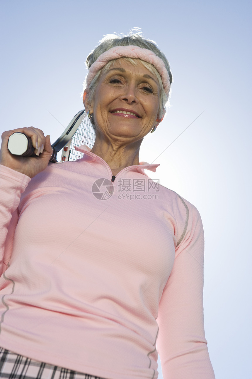 低角度的视角 快乐的年长妇女 拿着网球花架对着天空图片