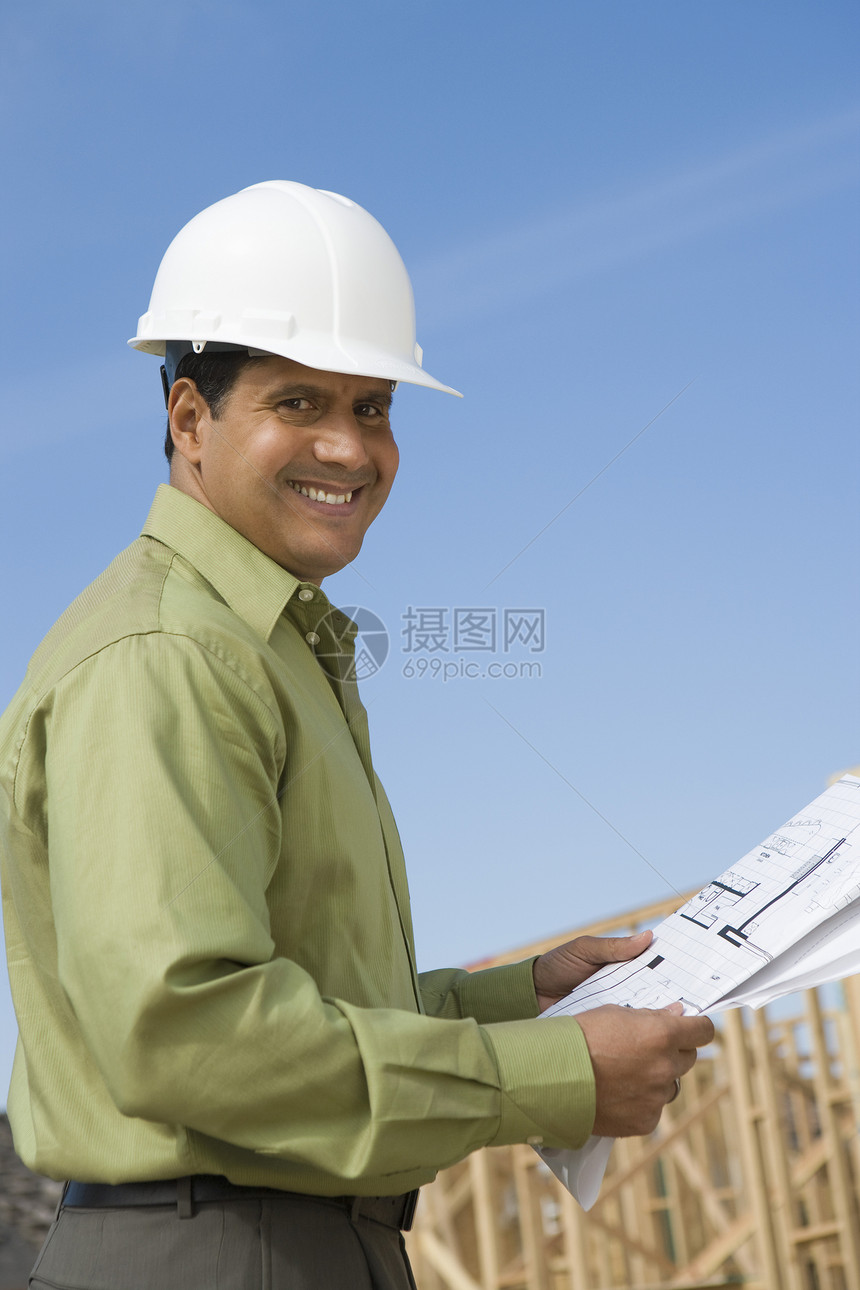 一位在建筑工地持有蓝图的快乐男性建筑师的肖像低角度职业中年眼神视图工作防护服安全帽男子图片
