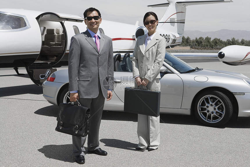 两位快乐的企业高管在机场站在一起 背景是汽车和飞机图片