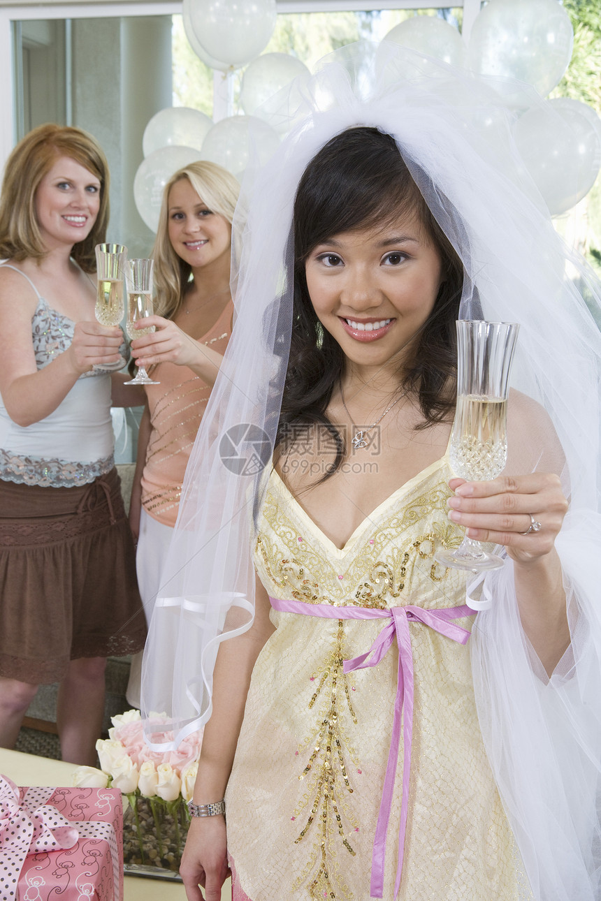 年轻快乐新娘的肖像与背景朋友一起拿着香槟笛子 在幕后图片