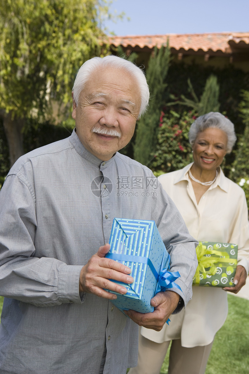 带着礼物的快乐老年男子肖像 与女性站在花园背景中 在花园里图片