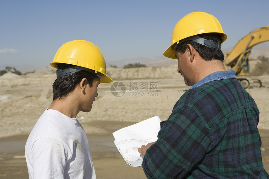 在建筑工地讨论蓝图的2名男性建筑设计师合作安全帽职业防护个人建筑工人团队中年阅读劳动图片