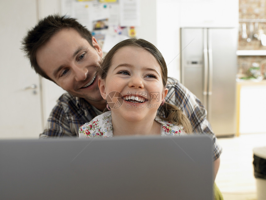 用笔记本电脑亲爱父亲和女儿 在家一起微笑图片
