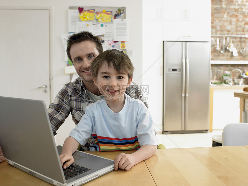 带着笔记本电脑坐在家里的桌子上 画着幸福的儿子和父亲的肖像图片