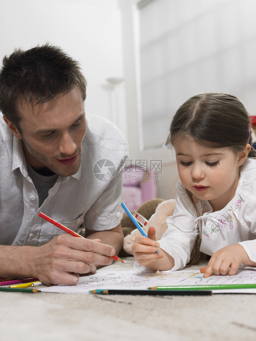父亲和女儿一起在家里的地板上染色书图片