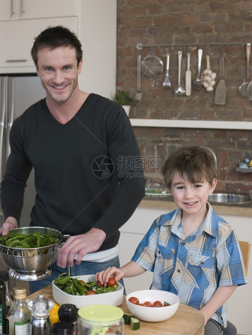快乐的父亲和儿子在厨房柜台一起准备沙拉的肖像图片