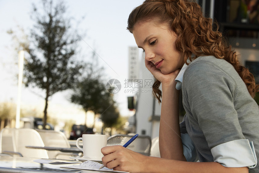 在户外咖啡厅纸面上写作的年轻女商务人士的侧面视图图片