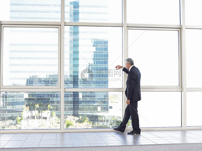 满身深思熟虑的商务人士站在办公大楼玻璃窗边站立图片
