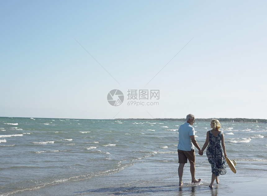 在热带海滩上手牵手行走的幸福老年情侣的近视婴儿娱乐男士退休假期团结乐趣夫妻女性太阳帽图片