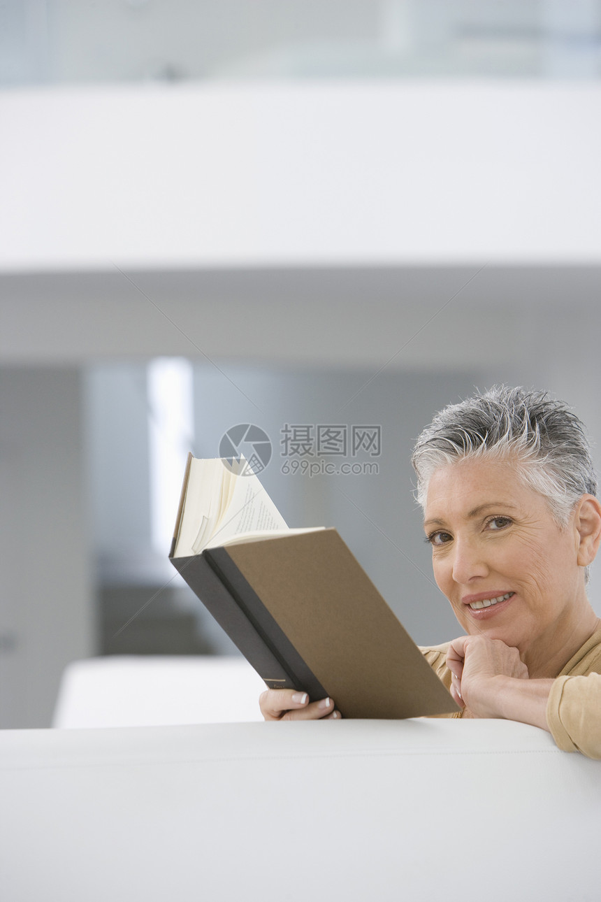 快乐的年长妇女在家沙发上读书的肖像退休短发公寓客厅中年爱好文学闲暇女性微笑图片