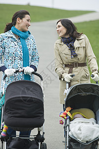 推童车快乐的年轻母亲在公园里推婴儿车聊天背景