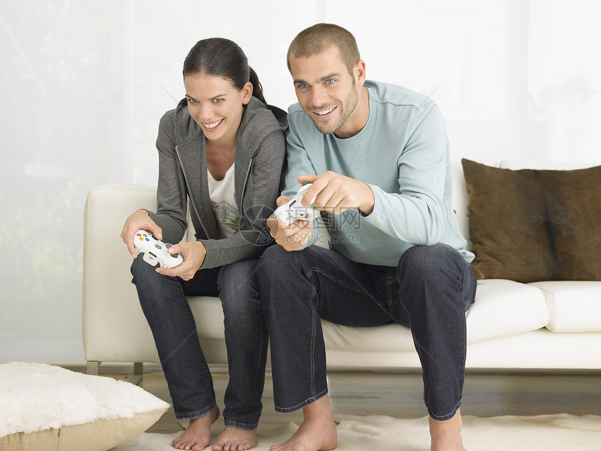 快乐的年轻夫妇在客厅沙发上玩电子游戏图片