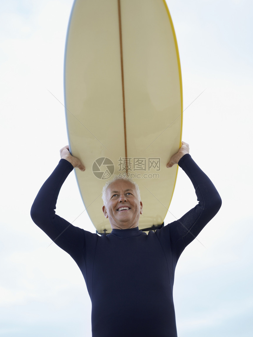 低角度的视角 微笑的老年男子带着冲浪板在头上对着天空图片
