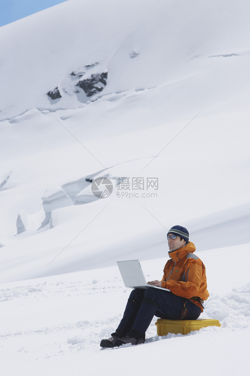 使用笔记本电脑在雪山景观上搭乘男性徒步旅行者的侧面视图远程工作荒野闲暇技术冒险风衣远足者远足上网图片