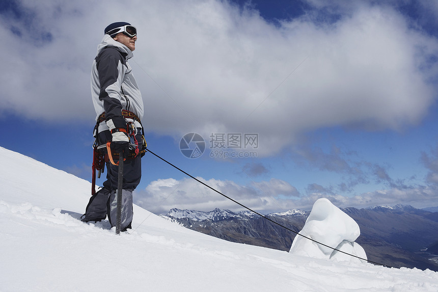 一名男性登山者在雪坡上站立的低角度视图 安全线附着勘探滑雪假期冬装成就风镜旅行探索者天空安全图片