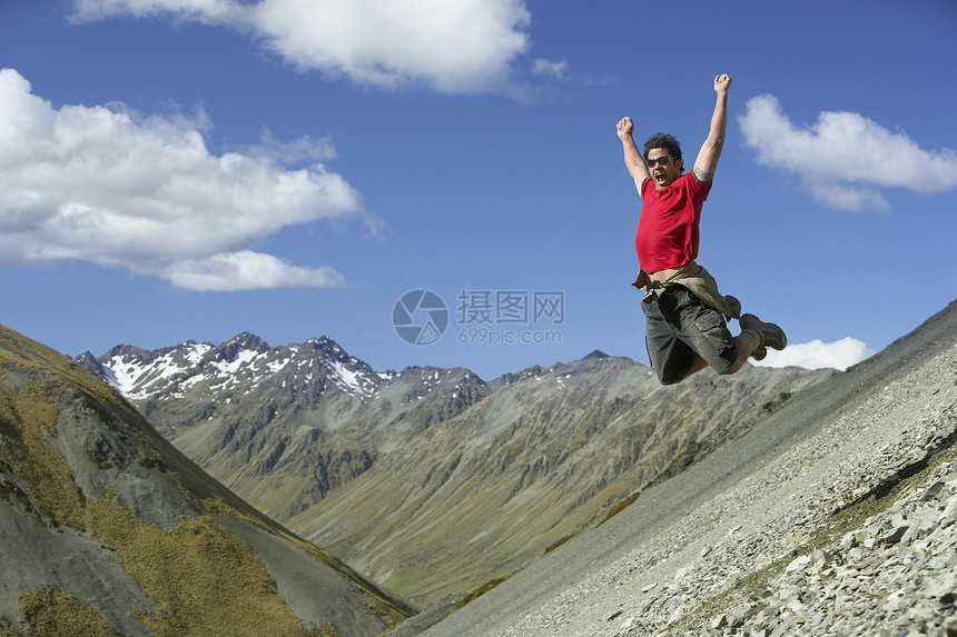 年轻人用举起的手臂跳下岩石坡图片