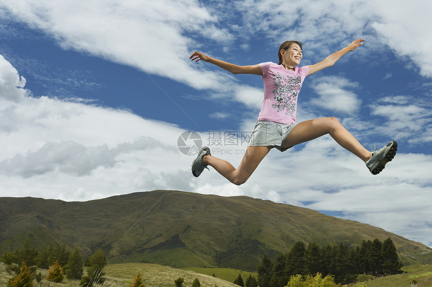 一名年轻妇女在农村地貌上跳跃的低角度视角女性天空乐趣娱乐活力假期场地爬坡风景幸福图片
