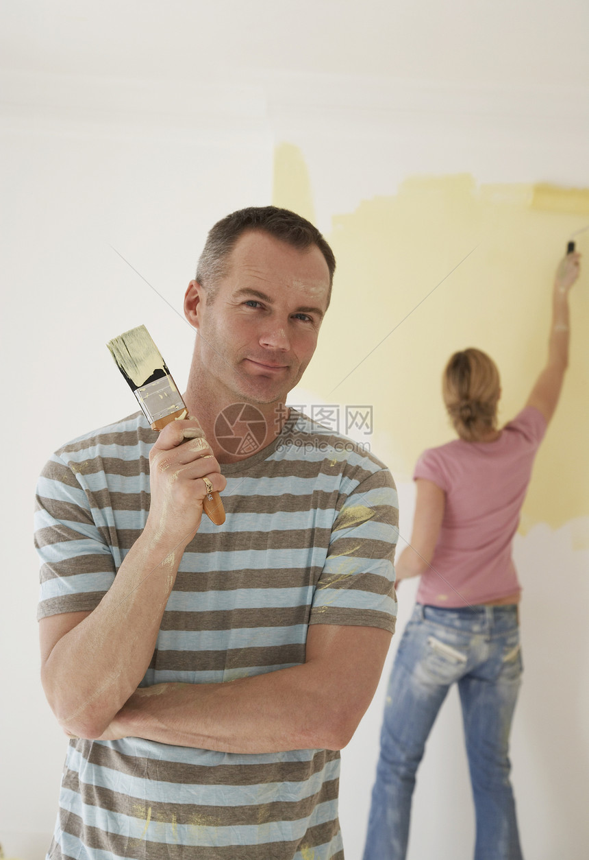 男人拿着油漆刷子 而女人在背景中画着滚滚的墙壁图片