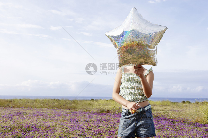 在花场站立时 将恒星形气球放在她面前的 早年女孩前视线图片