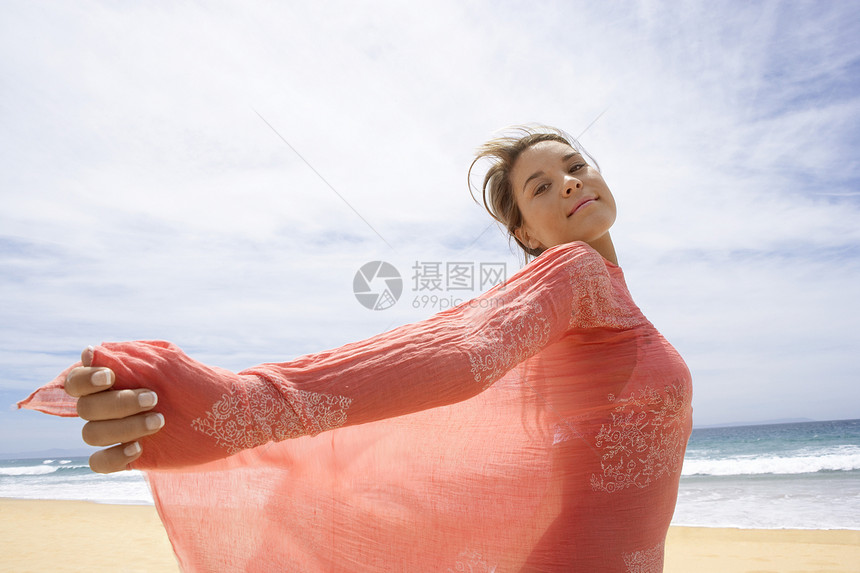 身着围巾站在海滩上的无忧无虑年轻女子的侧面肖像图片