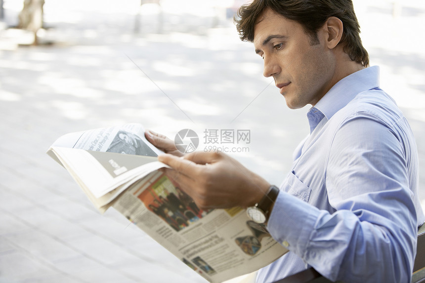 青年商务人士在户外长椅上阅读报纸的侧面视图图片