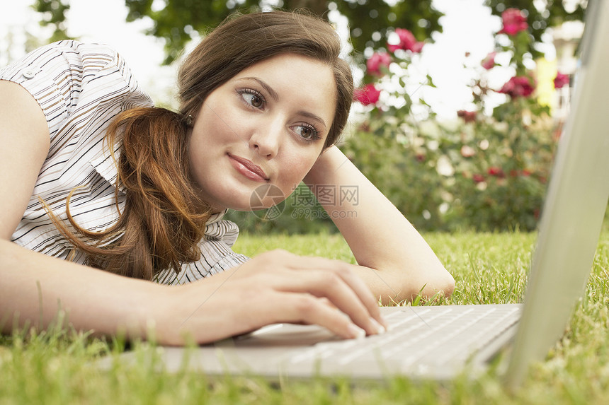 美丽的女商务人士在公园躺在草地上时使用笔记本电脑图片