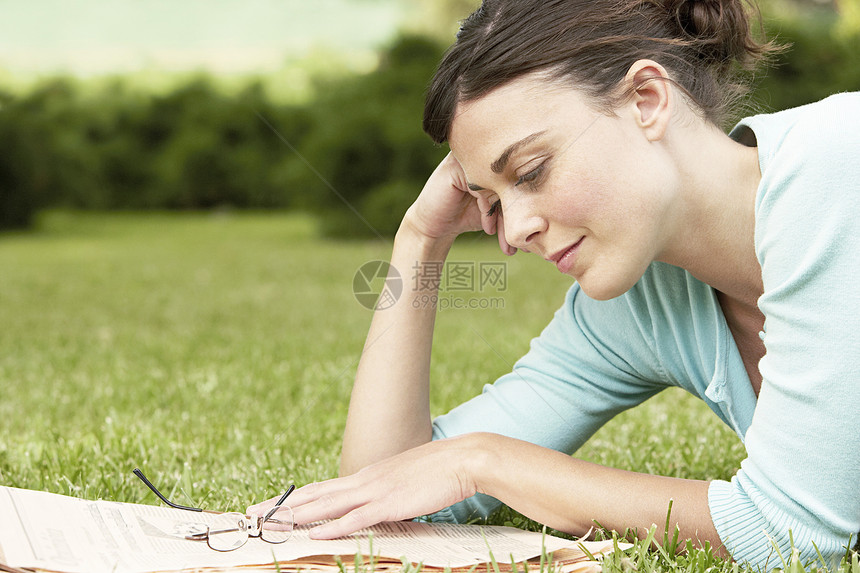 年轻女商务人士在公园躺在草地上看报纸时的侧面观图片