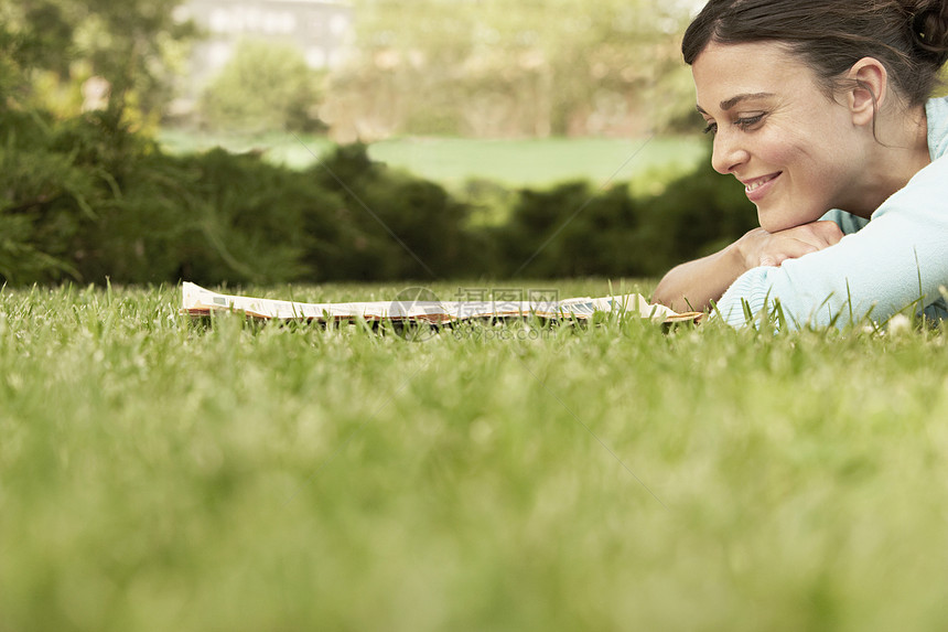 美丽的年轻女商务人士在公园的草地上躺着时 愉快地阅读报纸图片