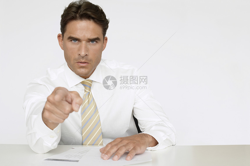 自信的商务人士在办公室白墙对面坐在办公桌边时指着他指着图片