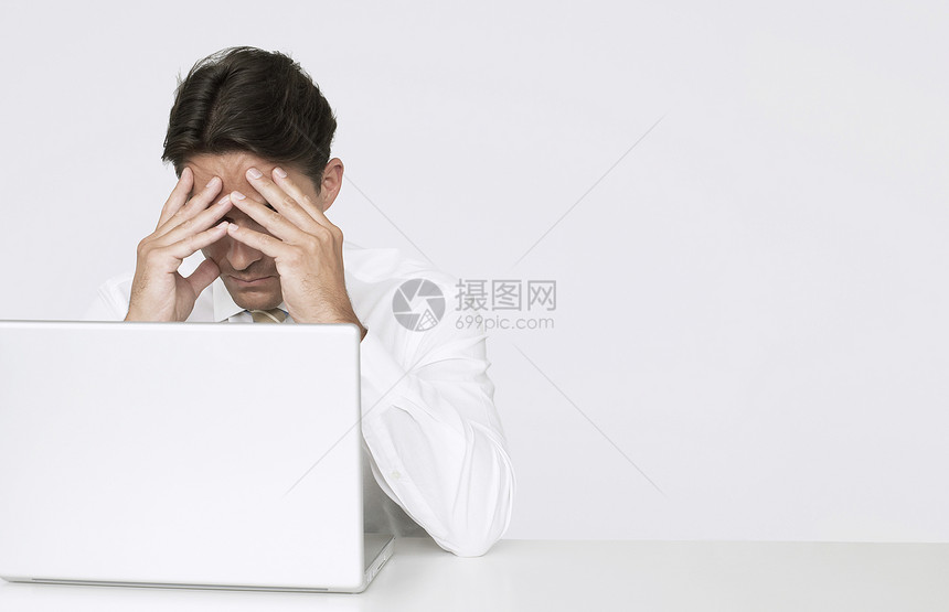 在办公室的白墙对面坐在桌子上用笔记本电脑坐在办公桌边 手持脸部的压抑商务人士图片