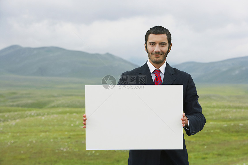 手持空白标志前视线的山田中站立着微笑的商务人士图片