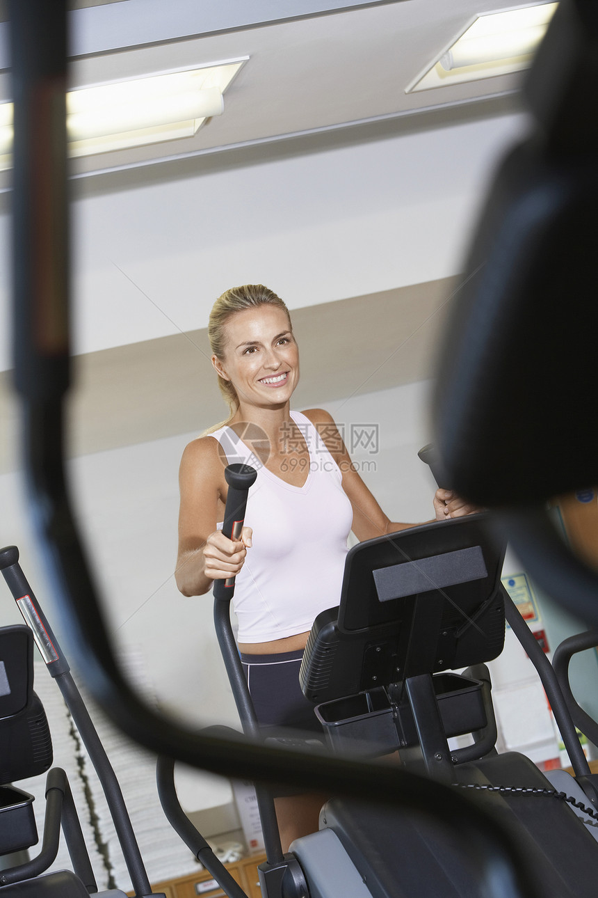 微笑的年轻女子在健身房用静灵机工作图片