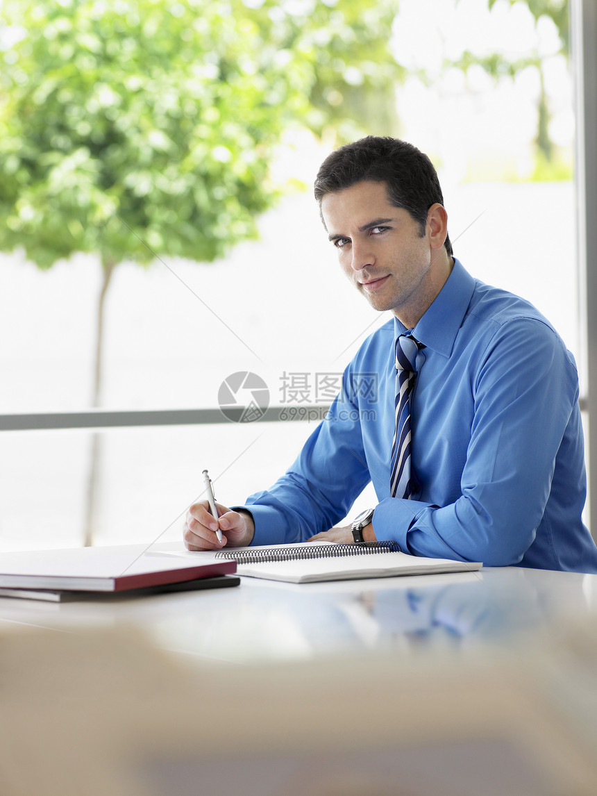 英俊青年商务人士在办公室服务台撰写笔记的肖像;图片