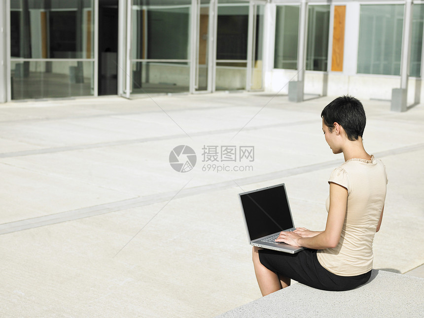 使用办公大楼外膝上型计算机的青年女商务人士图片