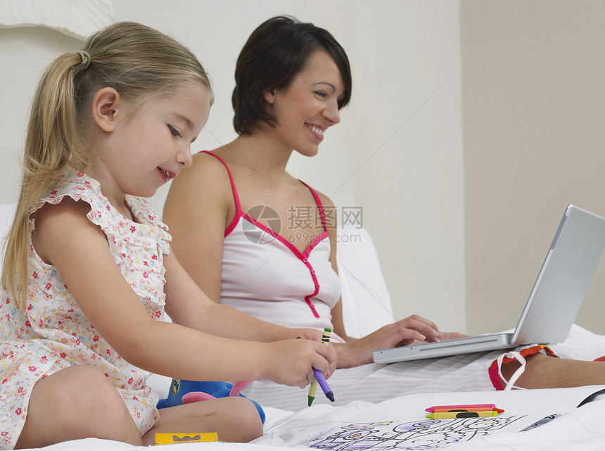 母亲在床上画画时使用女儿的笔记本电脑卧室计算房子家庭女士孩子女孩娱乐享受团结图片