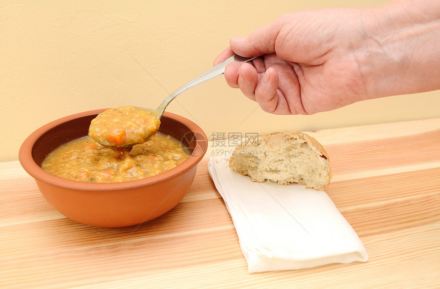 手握着汤汤汤勺 面包卷和餐巾在桌上图片