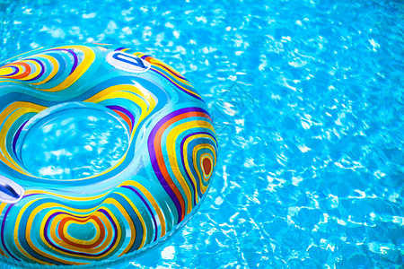 彩色漂浮圆圈漂浮在蓝游泳池中的可充气彩色橡胶环反射水池太阳问候紫色娱乐游泳玩具假期波纹背景