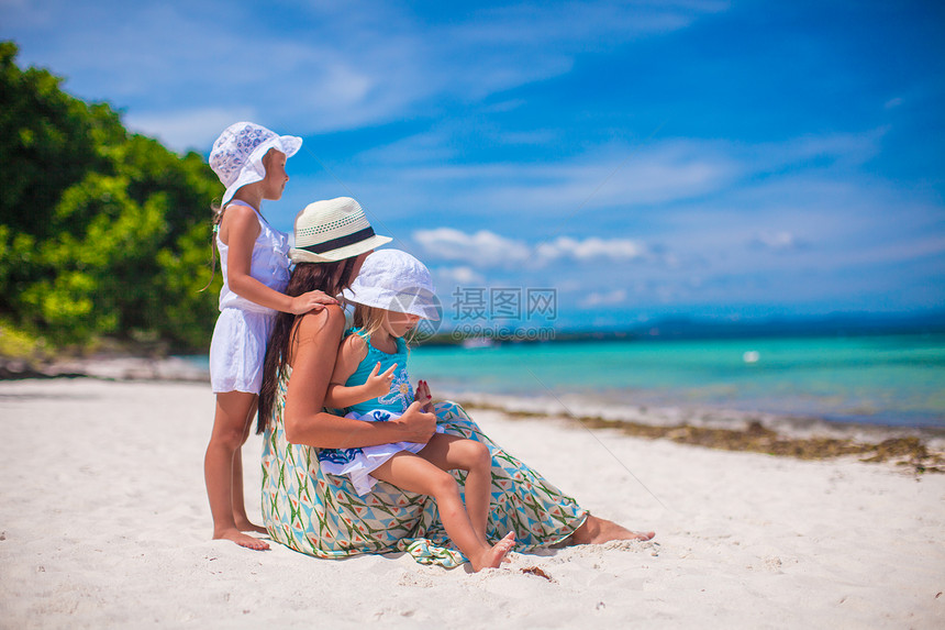 在阳光明媚的日落时尚年轻母亲 和两个孩子在奇异海滩上享受晴天海岸海滨异国帽子裙子妈妈家庭女士图片
