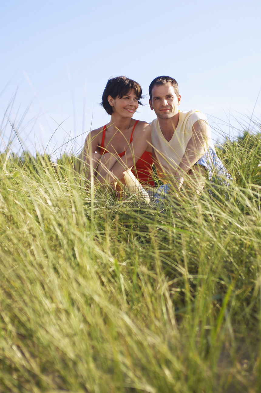 年轻浪漫情侣坐在沙滩高草地上女性微笑成人短发男人时间海滩感情假期女士图片