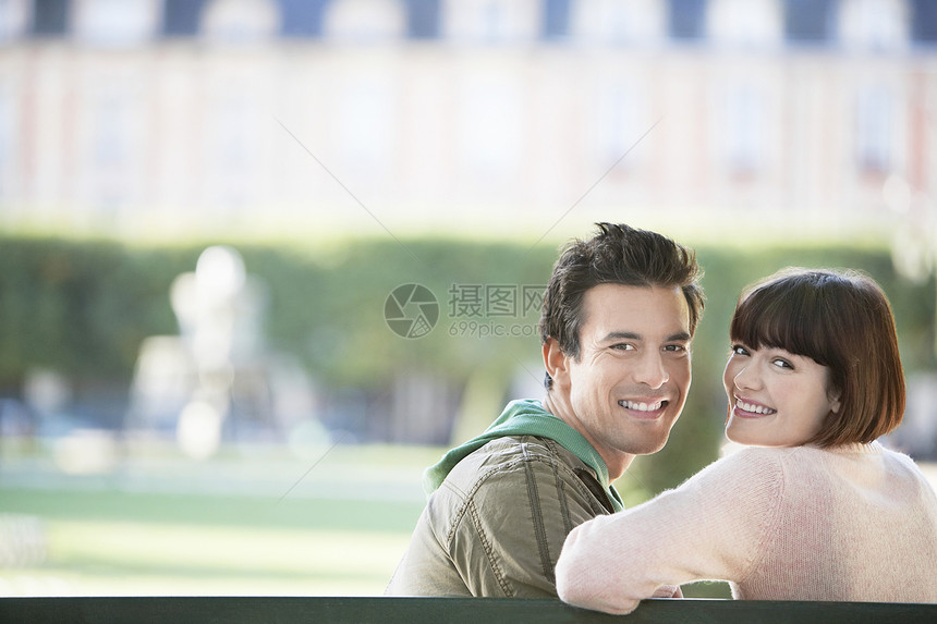 坐在公园长椅上的一对微笑的年轻夫妇的肖像图片