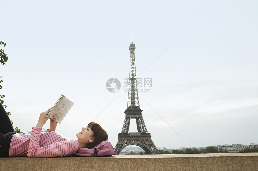 艾菲尔铁塔前 一位年轻女子躺在阳台上 阅读书的侧视角指南快乐观光地标成人享受女士闲暇旅游游客图片