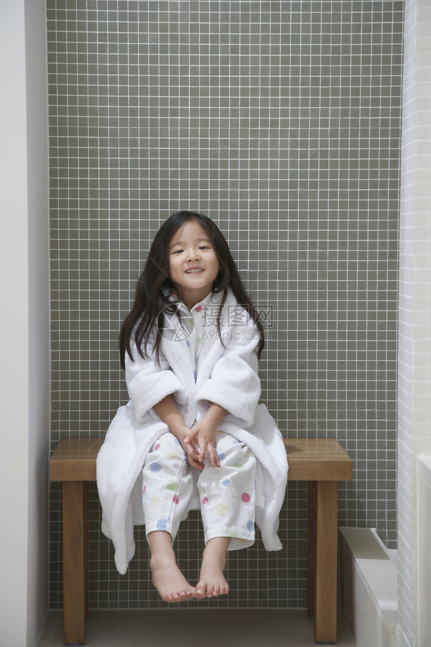 浴缸旁坐在长椅上的浴袍中一名年轻女孩的完整肖像图片