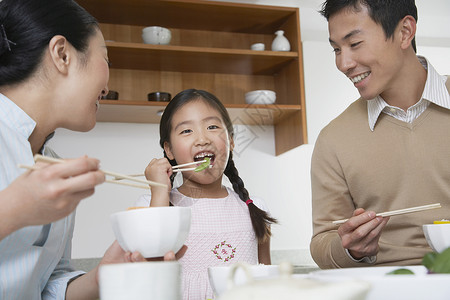 坐着吃饭的女孩年青夫妇和女儿在厨房用筷子吃饭背景
