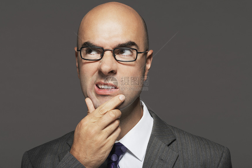 秃头商务人士戴眼镜 手在下巴上 脸在灰色背景下做笑脸图片