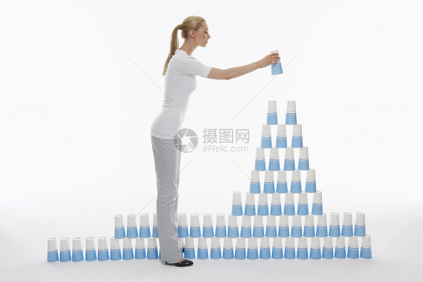 妇女用白色背景把塑料杯子叠成金字塔的全长侧视角图片