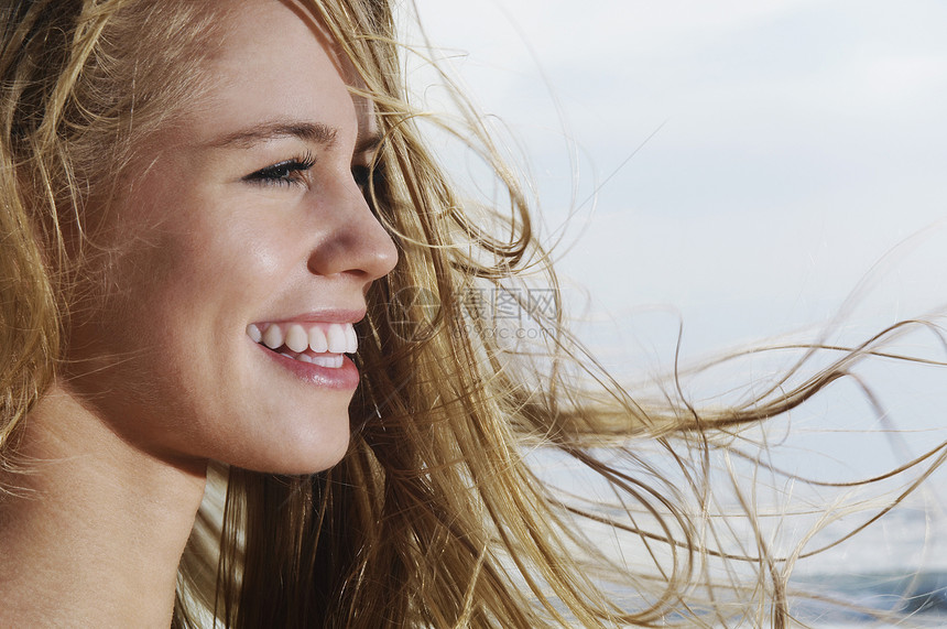 一个微笑的年轻女子 带着金发在风中吹着的头发向外看图片