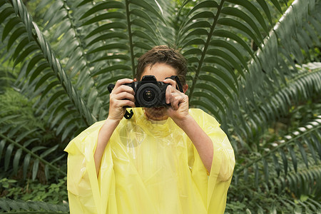 雨衣照片素材穿雨衣的年轻男孩在实地考察期间 在森林里拍照好奇心教育旅行植物树叶相机男性娱乐摄影叶子背景