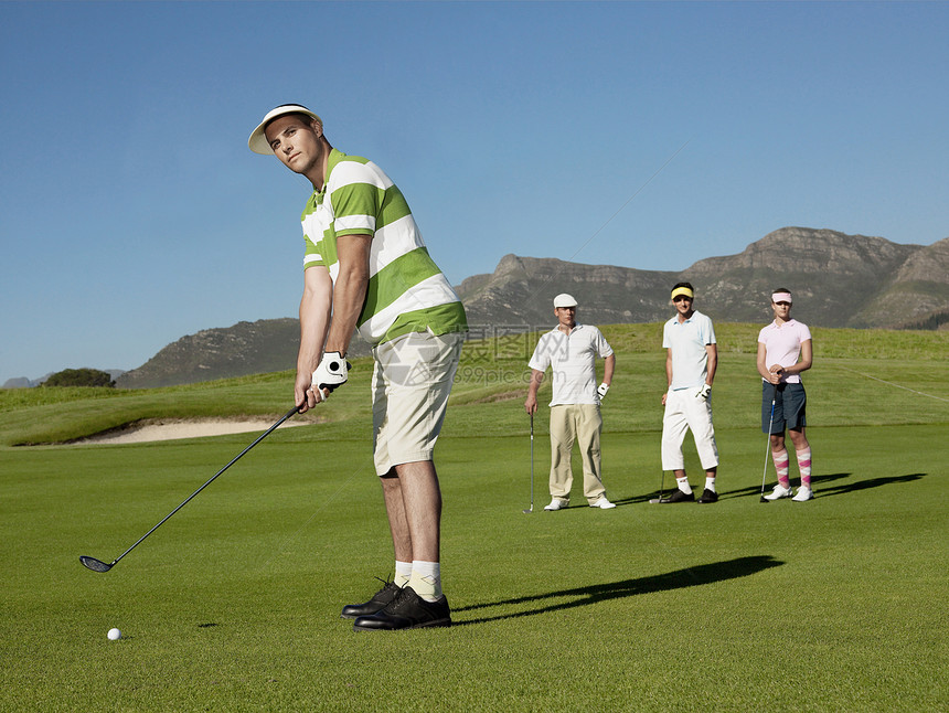 与背景竞争对手一起打高尔夫球的全年年轻男性高尔夫运动员图片