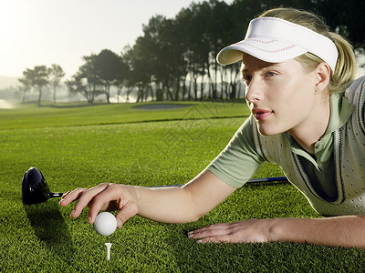 女子打高尔夫球美丽的年轻女子高尔夫运动员躺在草地上 同时在踢球场上打球背景