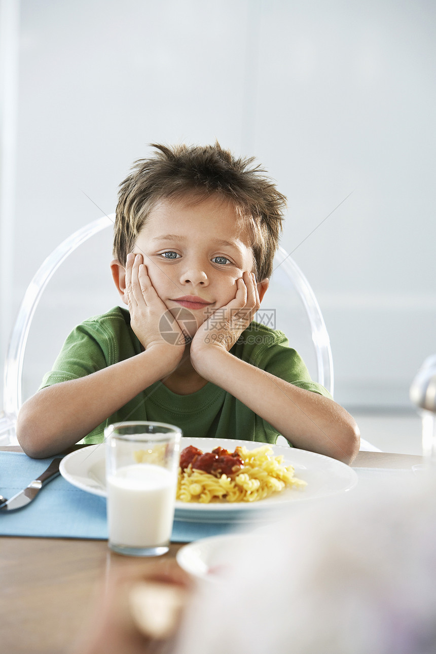 无聊的年轻男孩坐在早餐桌前的肖像图片